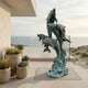 Large Contemporary Leaping Dolphins Bronze Sculpture by Giant Sculptures with verdigris patina, displayed on a coastal terrace beside potted succulents and ocean views.