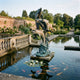 Giant Sculptures' 300cm Large Contemporary Leaping Dolphins Bronze Sculpture with verdigris patina, set on a wave base in a koi pond beside a balustrade in a walled garden.