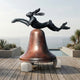 Giant Sculptures' 150cm Leaping Hare and Bell Bronze Sculpture with a black-green patinated hare above a reddish-brown bell, displayed on a poolside deck overlooking the sea.