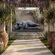 Large Contemporary Reclining Voluminous Female Figure Bronze Fountain by Giant Sculptures on a cascading stone base in a wisteria-draped courtyard.