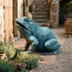 Large Contemporary Seated Frog Bronze Sculpture by Giant Sculptures with verdigris patina, mouth open skyward, set on a brick path beside a rustic doorway.