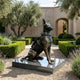 Large Contemporary Seated Military Working Dog Bronze Sculpture by Giant Sculptures, German Shepherd in tactical vest on granite plinth in a hedged garden.