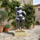 Large Contemporary Voluptuous Female Figure Bronze Sculpture by Giant Sculptures on a pale gold plinth in a Mediterranean courtyard with lavender and bougainvillea.