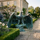 Large Heraldic Eagle Bronze Sculpture by Giant Sculptures with verdigris patina and outstretched wings, perched on a rocky base beside a rose-filled garden path.