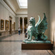 Large Heraldic Winged Lion-Dragon Gargoyle Bronze Sculpture by Giant Sculptures with verdigris patina, displayed on a wooden plinth in a museum gallery with paintings.