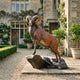 Large Traditional Bighorn Rams Bronze Sculpture by Giant Sculptures, reddish-brown patina ram with curled horns on a rocky base, displayed in a manor courtyard.