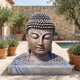 Large Traditional Buddha Head Bronze Bust by Giant Sculptures on a pale stone plinth in a Mediterranean courtyard with lavender, olive trees, and a pool.