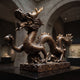 Large Traditional Coiling Chinese Dragon Bronze Sculpture by Giant Sculptures, shown in profile gripping a sphere on a cloud-scroll base in a museum hall.