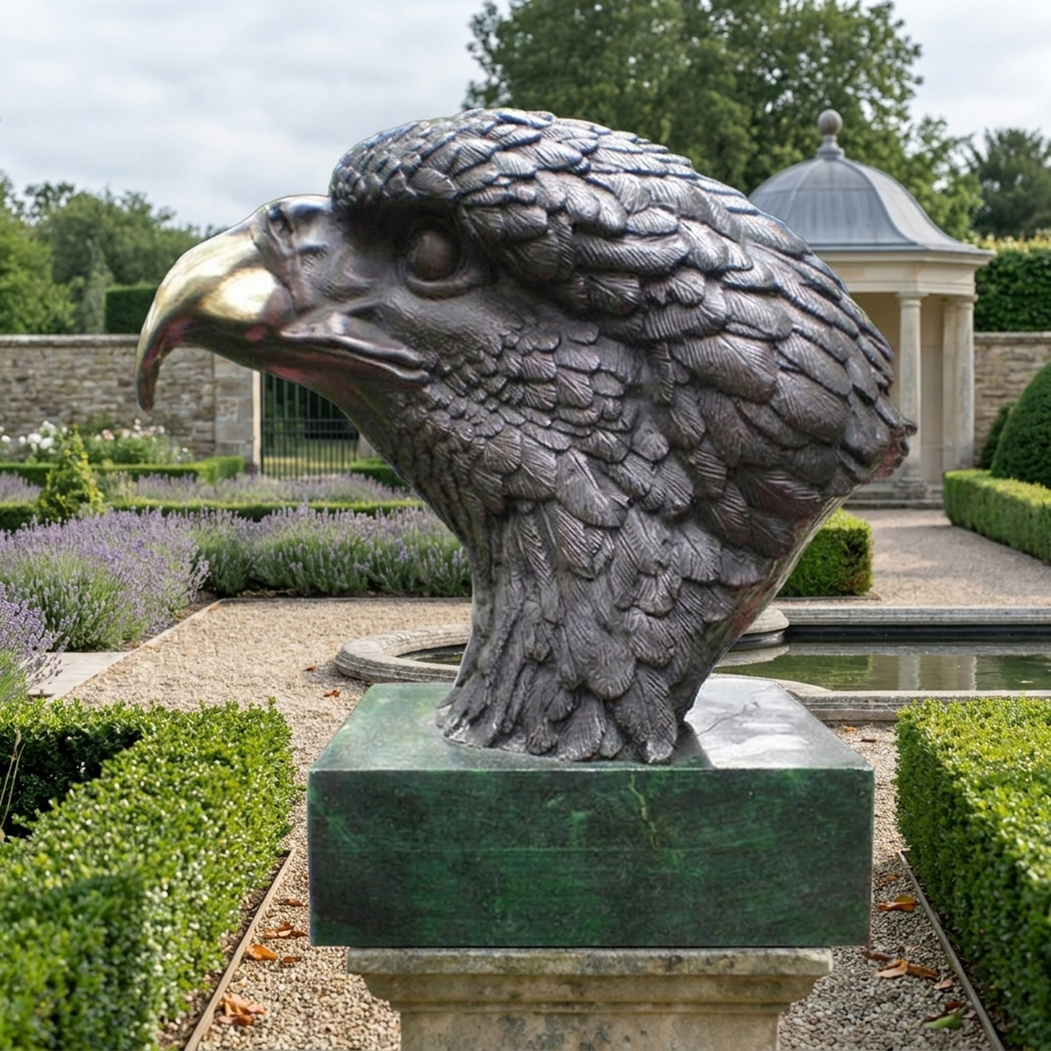 Large Traditional Eagle Head Bronze Bust by Giant Sculptures in profile with dark patina feathers and gold beak, on a green marble plinth in a formal garden.