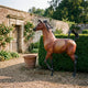 Large Traditional Prancing Arabian Horse Bronze Sculpture by Giant Sculptures with chestnut and black patina, displayed in a walled garden beside a hedge.