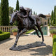 Large Traditional Racehorse and Jockey Bronze Sculpture by Giant Sculptures, shown mid-gallop on gravel beside a Mediterranean villa pool lined with cypress trees.