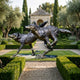 Large Traditional Running Wolves Bronze Sculpture by Giant Sculptures, two wolves mid-stride with dark patina, displayed in a formal hedged garden with cypress trees.