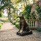 Large Traditional Seated Akita Dog Bronze Sculpture by Giant Sculptures, 150cm, on a stone garden terrace beside a brick wall and lavender-lined path.