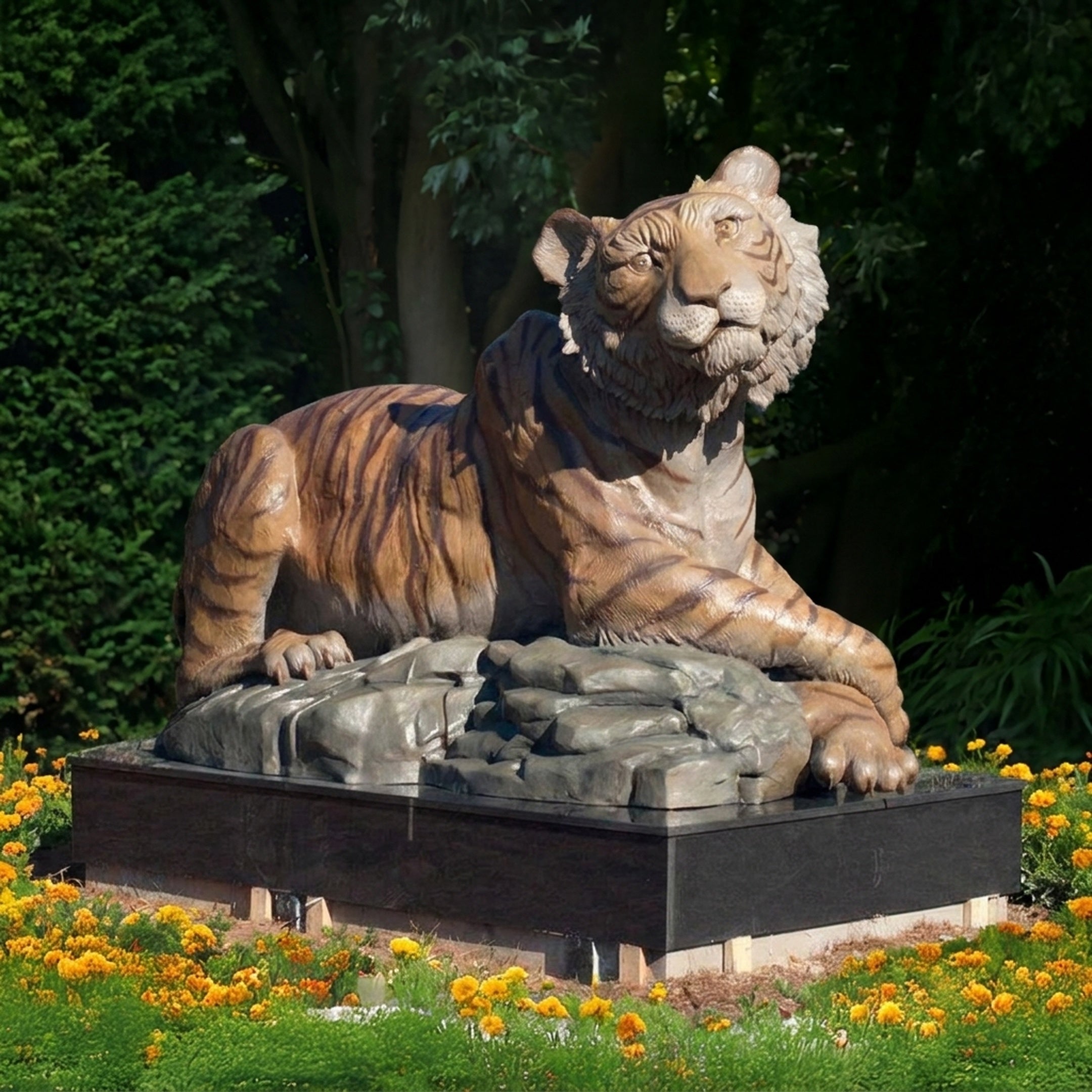 Large Traditional Seated Tiger Bronze Sculpture by Giant Sculptures in polychrome orange and black on a grey rock base, displayed outdoors among marigolds.