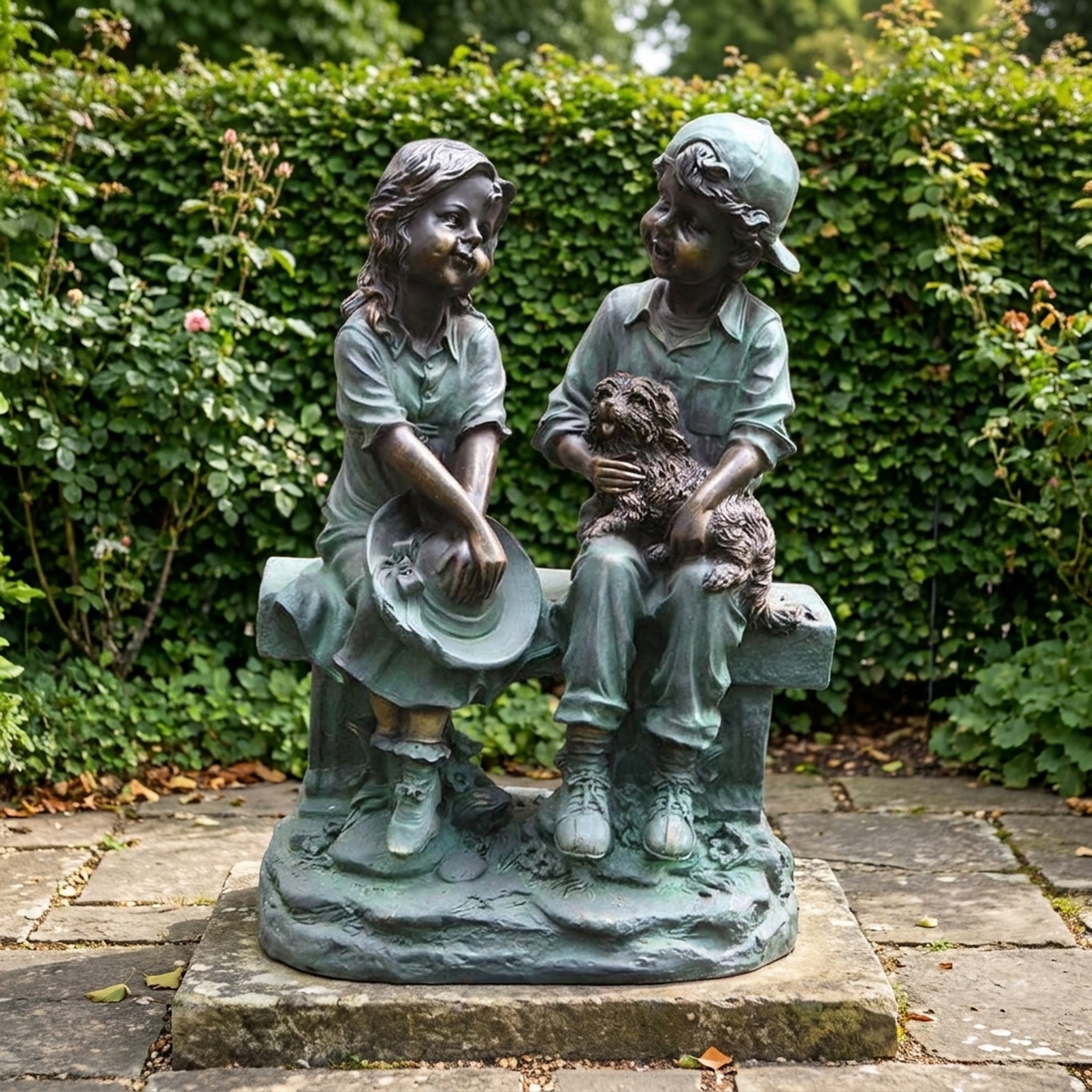 Large Traditional Two Children and Dog Bronze Sculpture by Giant Sculptures, verdigris finish, shown on a garden patio before a green hedge.
