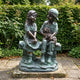 Large Traditional Two Children and Dog Bronze Sculpture by Giant Sculptures, verdigris finish, shown on a garden patio before a green hedge.