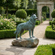 Life-Size Alert Husky Dog Bronze Sculpture by Giant Sculptures with verdigris patina on a boulder base, displayed on a formal garden path with topiary and stone archway.