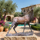 Life-Size Bugling Bull Elk Bronze Sculpture by Giant Sculptures, 230cm, displayed on a stone plinth in a Mediterranean courtyard with olive trees and pool.