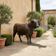 Life-Size Charging Bull Bronze Sculpture by Giant Sculptures in dark patina, displayed on a stone terrace beside olive trees and lavender along a villa pathway.