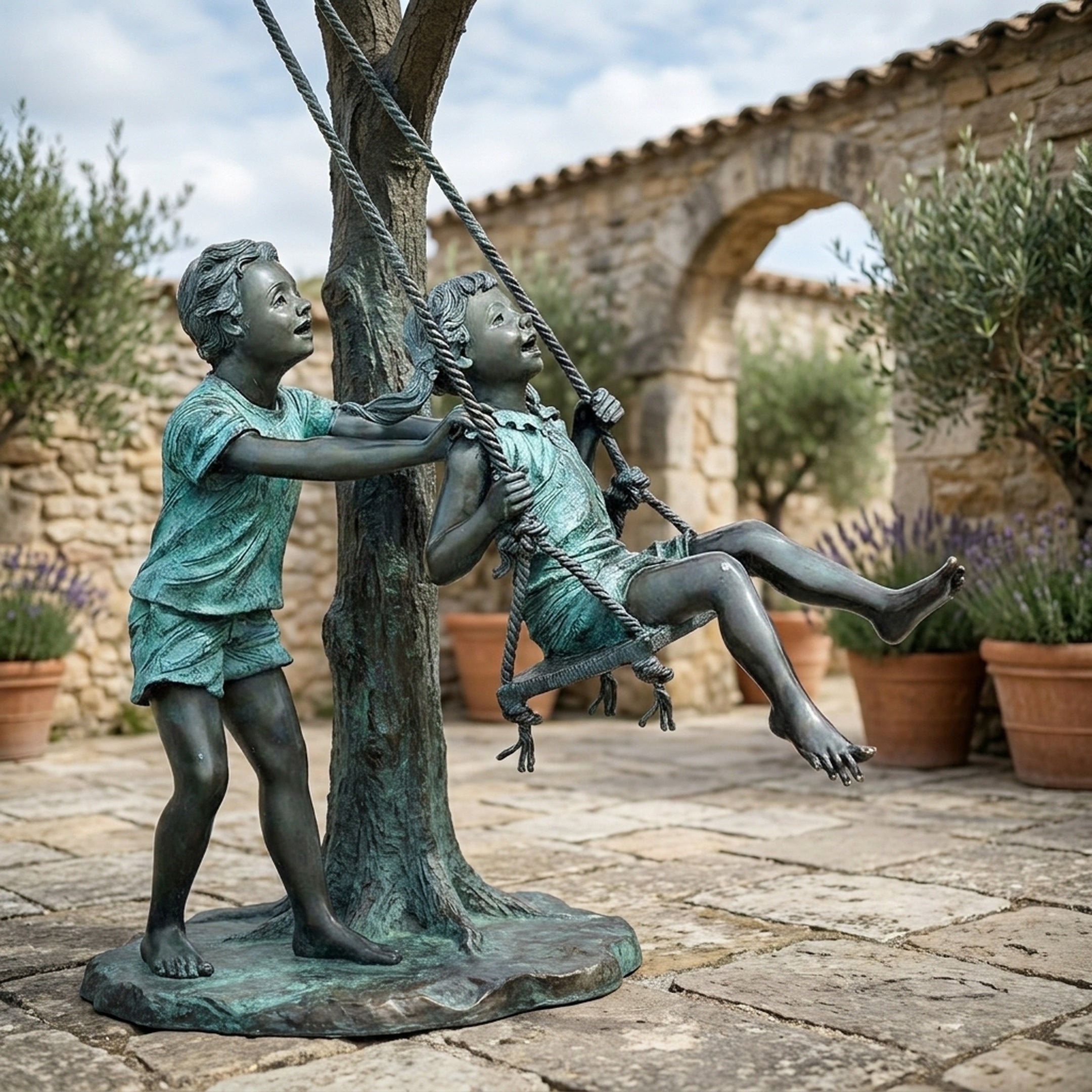 Life-Size Children on Swing Bronze Sculpture by Giant Sculptures, verdigris-patinated boy pushing a girl on a rope swing tied to a tree, in a stone courtyard.
