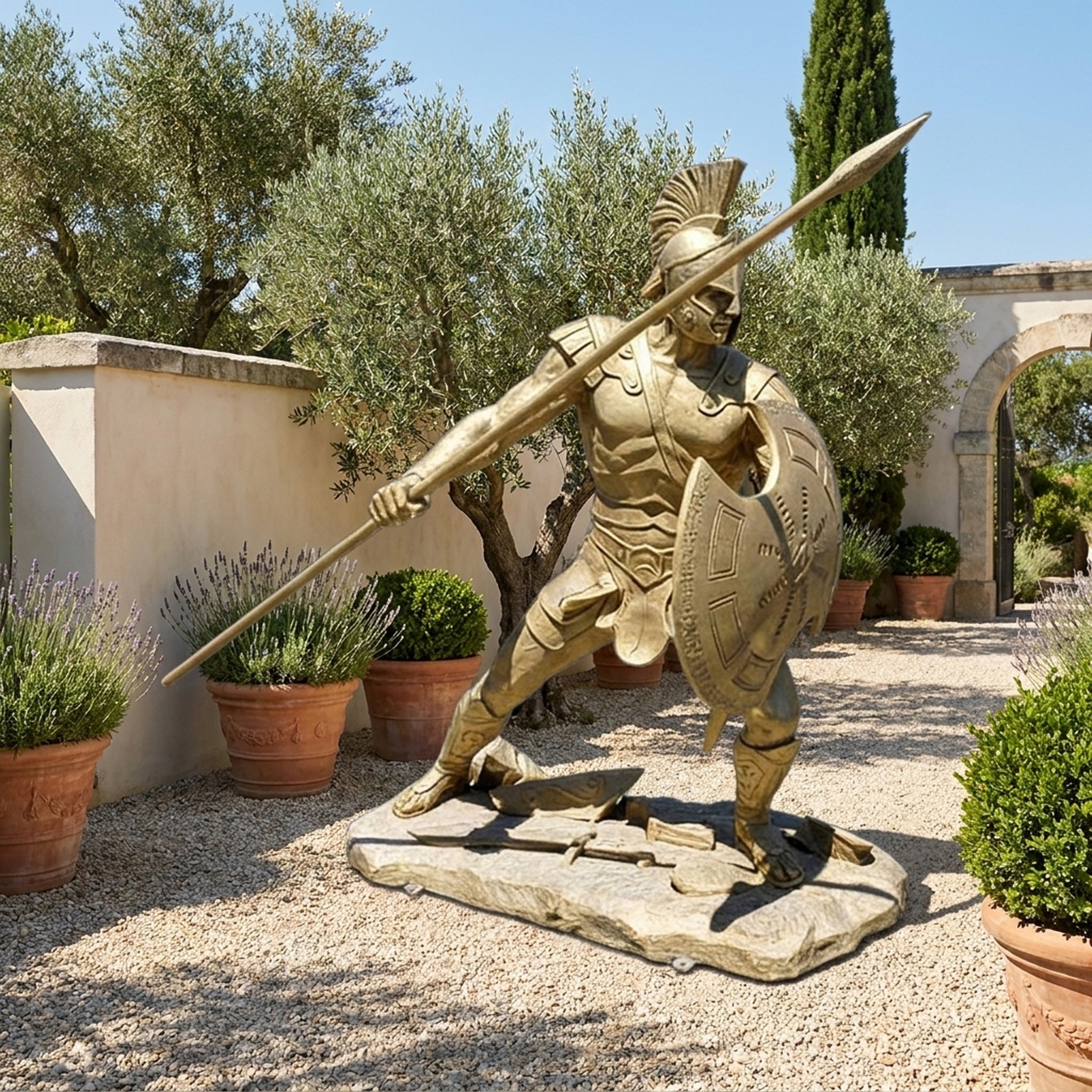 Giant Sculptures Life-Size Classical Ancient Warrior Bronze Statue in polished gold, lunging with spear and shield, displayed on gravel in a Mediterranean garden.
