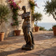 Life-Size Classical Armless Goddess Bronze Statue by Giant Sculptures on a terracotta-tiled Mediterranean terrace with olive trees, bougainvillea, and sea view.
