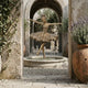 Life-Size Classical Ballerina Dancer Bronze Fountain by Giant Sculptures in arabesque en pointe within a circular stone basin, framed by a stone archway.