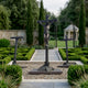 Life-Size Classical Crucifixion of Christ Bronze Sculpture by Giant Sculptures, dark patina three-cross Calvary set on gravel in a boxwood parterre garden.