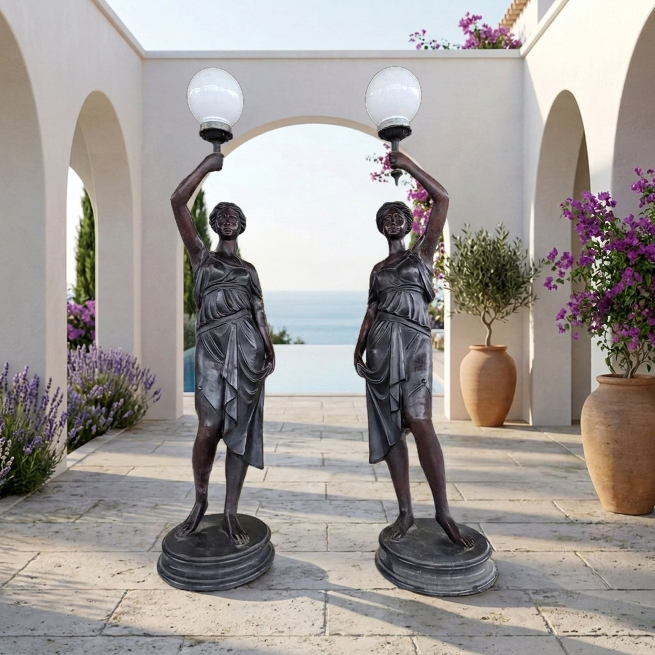 Pair of Giant Sculptures Life-Size Classical Draped Female Figure Lamp Bronze Sculptures with white globe lamps, displayed in an arched Mediterranean courtyard.