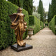 Giant Sculptures Life-Size Classical Female Angel Bronze Sculpture in warm gold patina on a dark plinth, displayed on a gravel path between hedges and cypress trees.