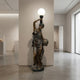 Life-Size Classical Female Figure Bronze Sculpture by Giant Sculptures, 230cm draped goddess holding a frosted globe lamp aloft and a basket, in a gallery.