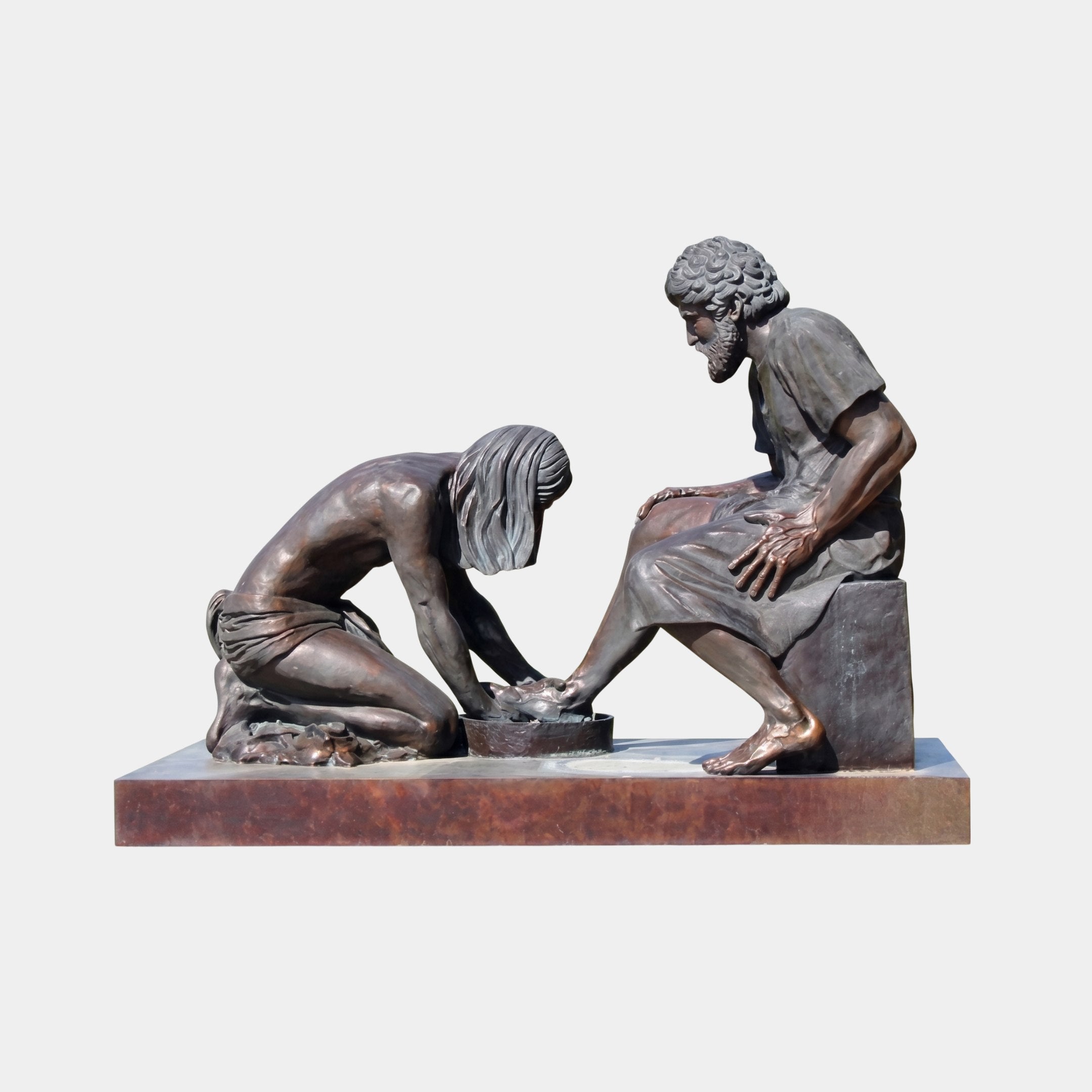 Life-Size Classical Foot-Washing Scene Bronze Sculpture by Giant Sculptures, showing a kneeling figure washing the feet of a seated bearded man on a reddish-brown plinth.