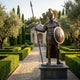 Life-Size Classical Greek Warrior Bronze Sculpture by Giant Sculptures, 250cm Spartan figure with crested helmet, spear and round shield, on a plinth in a formal garden.