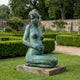 Life-Size Classical Kneeling Female Figure Bronze Sculpture by Giant Sculptures in verdigris patina, displayed on a stone plinth in a formal hedged garden.