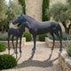 Life-Size Classical Mare and Standing Foal Bronze Sculpture by Giant Sculptures, dark patinated horses on ground pins in a Mediterranean garden with lavender and cypress.