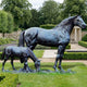 Life-Size Classical Mare and Foal Bronze Sculpture by Giant Sculptures, dark patina mare standing beside grazing foal on a naturalistic base in a formal garden.