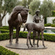 Life-Size Classical Mare and Foal Bronze Sculpture by Giant Sculptures, showing the mare bowing toward the foal beside a standing female figure in a garden.