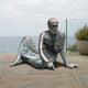 Life-Size Classical Reclining Bearded Scholar Bronze Sculpture by Giant Sculptures, shown on stone paving by a glass railing with the ocean behind.