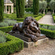 Life-Size Classical Reclining Lion Bronze Sculpture by Giant Sculptures with dark patina, resting on a stone plinth in a formal garden with cypress trees and lavender.