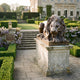 Giant Sculptures Life-Size Classical Recumbent Lion Bronze Sculpture 140cm on a weathered stone plinth beside steps in a formal manor garden at dusk.