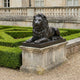 Life-Size Classical Recumbent Lion Bronze Sculpture by Giant Sculptures in dark patina, displayed on a stone plinth beside manicured hedges at a grand estate.