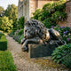 Life-Size Classical Recumbent Lion Bronze Sculpture by Giant Sculptures resting on its plinth along a gravel garden path beside hydrangeas and a manor house.