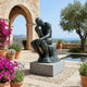 Life-Size Classical Seated Male Figure Bronze Sculpture by Giant Sculptures with verdigris patina, displayed on a grey plinth in a Mediterranean courtyard beside a pool.