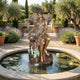 Life-Size Classical Seated Woman Pouring Water Bronze Fountain by Giant Sculptures in a Mediterranean garden pond with water lilies, lavender, and olive trees.