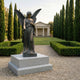Life-Size Classical Standing Angel Bronze Sculpture by Giant Sculptures on a stepped granite plinth in a formal cypress-lined garden with a classical pavilion behind.