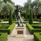 Life-Size Classical Standing David Bronze Statue by Giant Sculptures on a stone plinth, displayed along a gravel path in a formal boxwood garden.