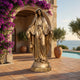 Life-Size Classical Virgin Mary Bronze Statue 220cm by Giant Sculptures in golden patina, arms open in blessing, on Mediterranean terrace with bougainvillea and sea view.
