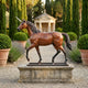 Life-Size Classical Walking Unicorn Bronze Sculpture by Giant Sculptures on a stone plinth, displayed on a gravel path lined with cypress trees and lavender.