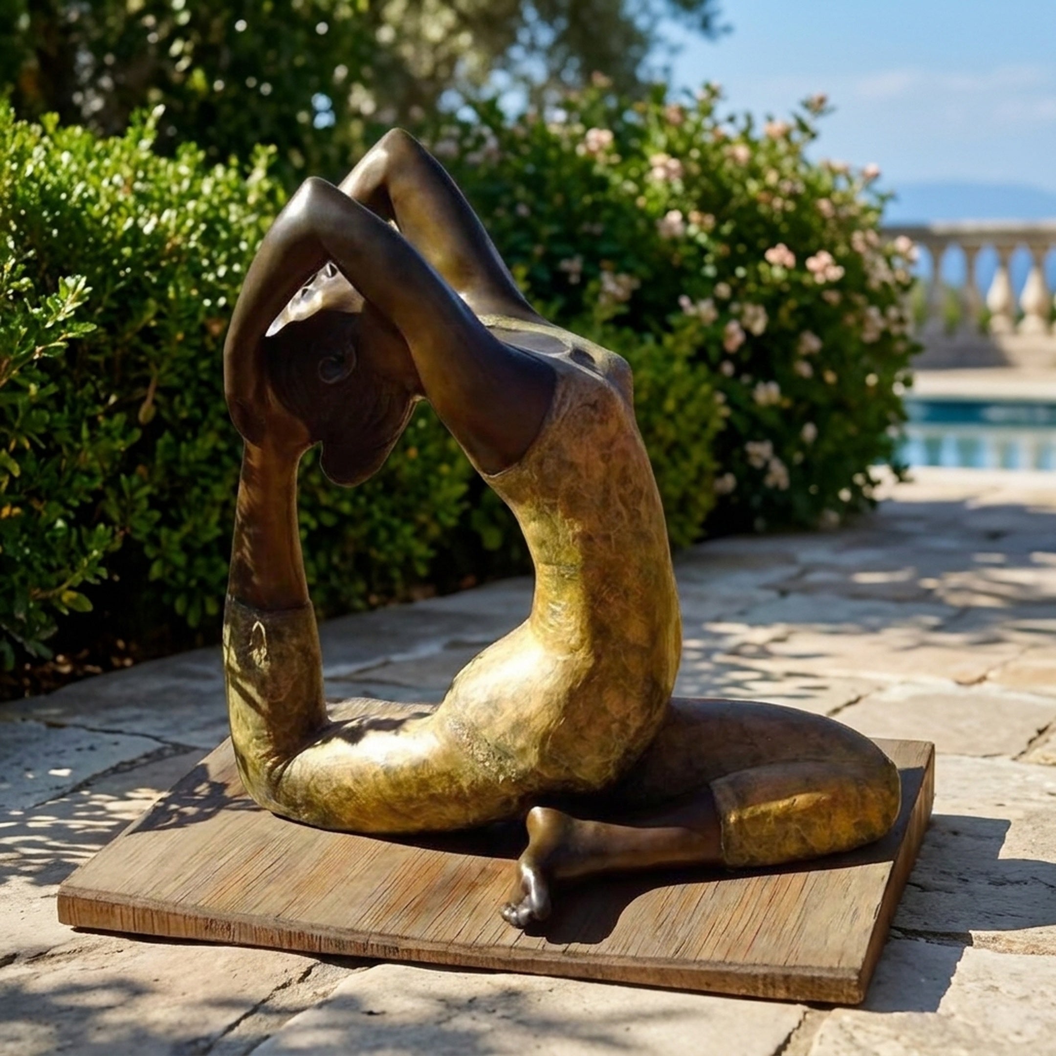 Giant Sculptures Life-Size Contemporary Backbend Figure Bronze Sculpture on a wooden base, displayed on a stone terrace beside greenery and a pool.