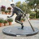 Life-Size Contemporary Baseball Player Bronze Statue by Giant Sculptures, mid-stride with bat angled down, on a circular granite plinth in a Mediterranean courtyard.